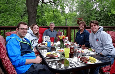 AJ's family gathered around a table outdoors eating dinner.