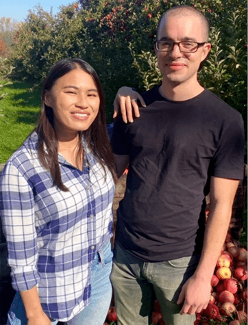 A photo of Caitlin standing next to her fiancé in an apple orchard.