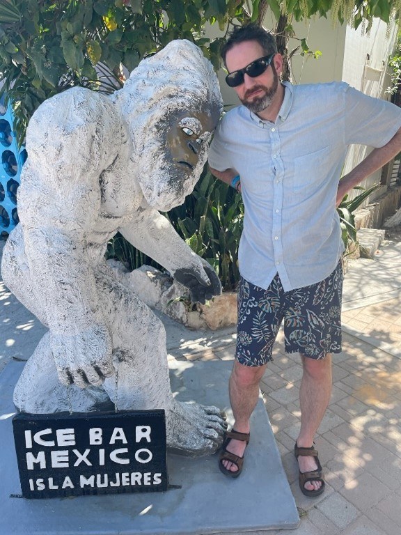 David standing next to a sculpture of Sasquatch with a sign in front of it that reads "Ice Bar Mexico Isla Mujeres"