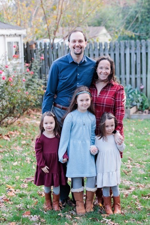 Justin, his wife, and his three daughters posing in their backyard for a family picture.